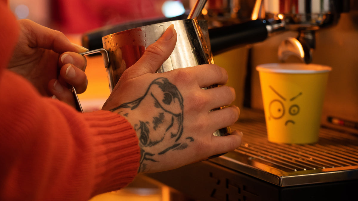 Barista in Bad Coffee Hackney Wick with a cow tattoo on her han steaming milk from Northiam Farm Dairy