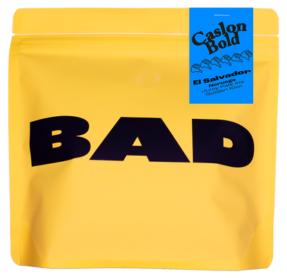 Yellow specialty coffee bag with 'BAD' in black text and a blue label stating "Caslon Bold, El Salvador, Noruega, Juicy Pale Ale and Golden Kiwi"