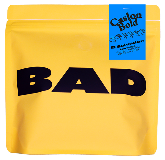 Yellow specialty coffee bag with 'BAD' in black text and a blue label stating "Caslon Bold, El Salvador, Noruega, Juicy Pale Ale and Golden Kiwi"