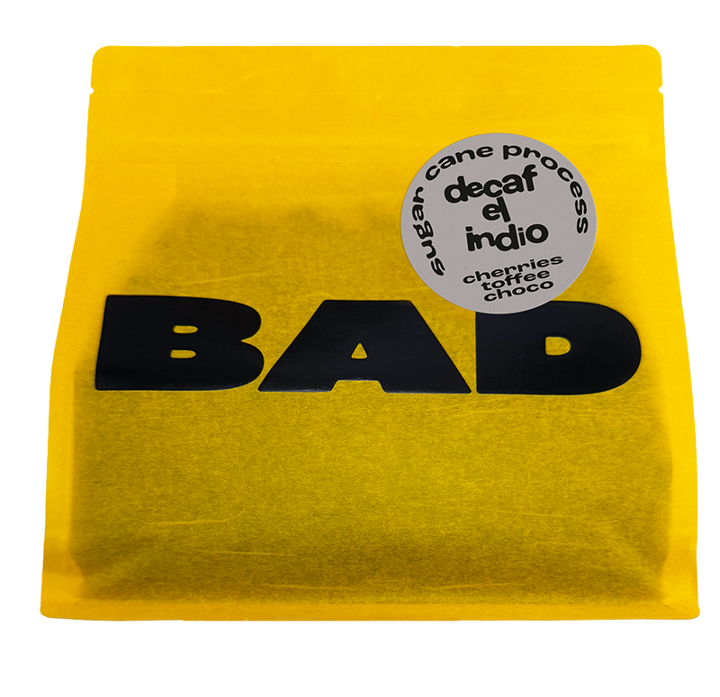 A bright yellow stand-up pouch of decaf coffee with bold black 'BAD' lettering and a round grey label reading 'decaf el indio' and 'chocolate toffee choco'.