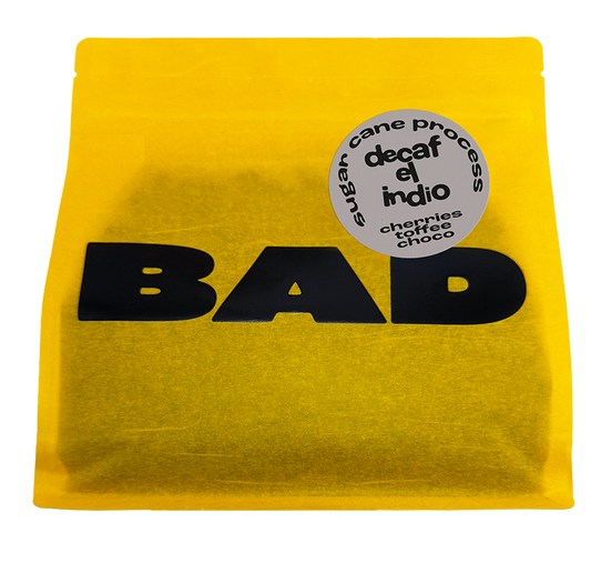 A bright yellow stand-up pouch of decaf coffee with bold black 'BAD' lettering and a round grey label reading 'decaf el indio' and 'chocolate toffee choco'.