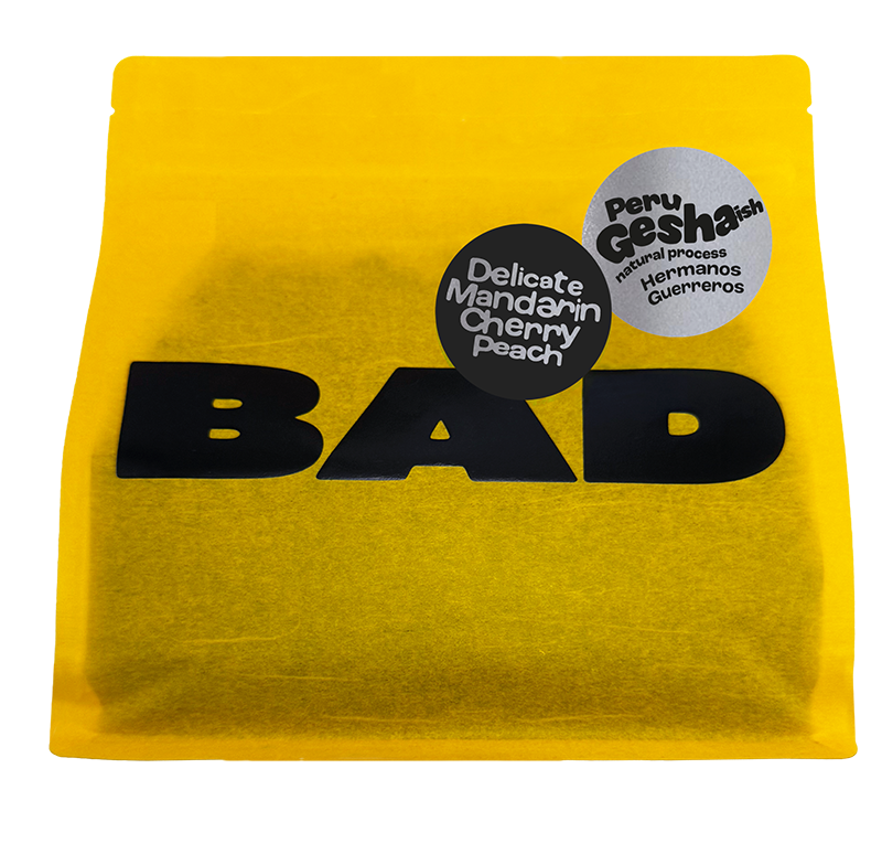 A bright yellow pouch of Peru Gesha Coffee with taste notes of 'Delicate Mandarin Cherry Peach' coffee, featuring a bold black 'BAD Coffee' logo and two circular product labels on the front.