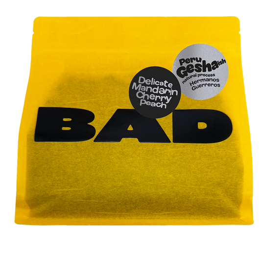 A bright yellow pouch of Peru Gesha Coffee with taste notes of 'Delicate Mandarin Cherry Peach' coffee, featuring a bold black 'BAD Coffee' logo and two circular product labels on the front.