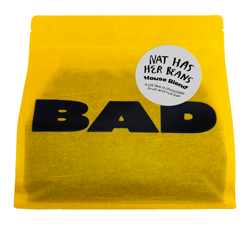 A bright yellow stand-up pouch of coffee beans with large black 'BAD' lettering and a round white sticker reading 'NAT HAS HER BEANS House Blend' on a plain white background.