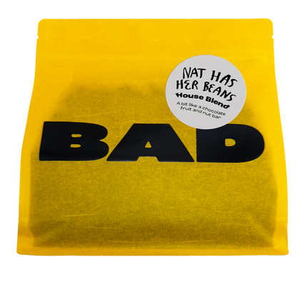 A bright yellow stand-up pouch of coffee beans with large black 'BAD' lettering and a round white sticker reading 'NAT HAS HER BEANS House Blend' on a plain white background.