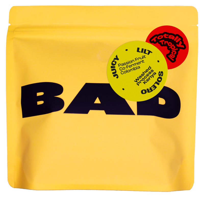 A yellow stand-up pouch of coffee with large black 'BAD' lettering and two circular flavor stickers reading 'Totally Tropicale' and 'Passion Fruit Co-Fermented coffee'.